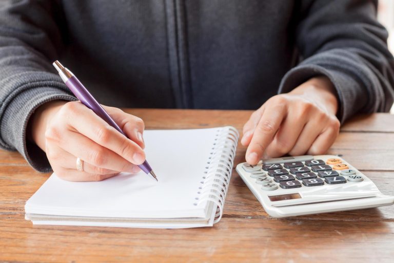 person-writing-in-a-notebook-with-a-calculator-free-photo